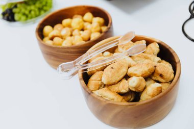 Küçük, lezzetli, gevrek kruvasanlar ahşap bir tabakta yatıyor. Tabağın üstünde onlar için maşa var..