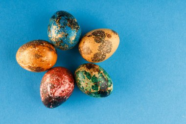  Mavi, yeşil, kırmızı ve sarı renklerle boyanmış beş paskalya yumurtası daire şeklinde uzanır. Mavi arka planda boyanmış paskalya yumurtaları. Düz yatıyordu. Uzayı kopyala Kapat. .