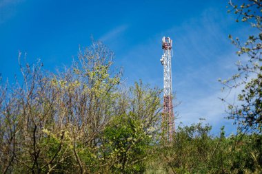 Telekomünikasyon kulesi 4G ve 5G hücresel. Hücre Alanı Üs İstasyonu. Kablosuz İletişim Anten Vericisi. Mavi gökyüzü ve ağaç zeminine karşı antenli telekomünikasyon kulesi. 