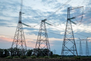 Elektrik direkleri ve günbatımı arka planında yüksek voltajlı elektrik hatları. İletim kulelerinin grup silueti