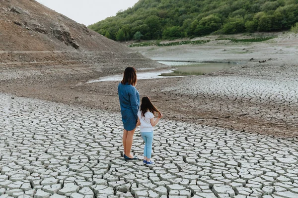 一个女人和一个女孩手拉手站在干裂的地上 看着干涸的湖面 全球变暖 — 图库照片