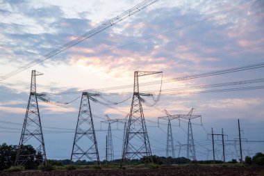 Elektrik direkleri ve günbatımı arka planında yüksek voltajlı elektrik hatları. İletim kulelerinin grup silueti