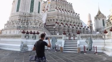Genç bir adam Wat Arun 'un yanında yürüyor ve akıllı telefondan video çekiyor. Bangkok,