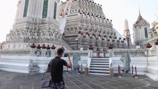 Een jongeman loopt in de buurt van Wat Arun en maakt een video op een smartphone. Bangkok, — Stockvideo