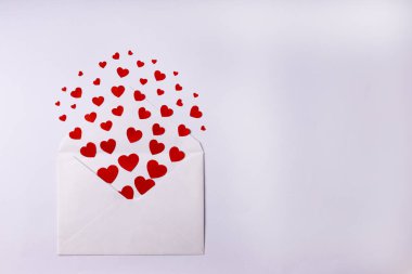 Beyaz zemin üzerinde kırmızı küçük kağıt kalpler olan beyaz bir zarf. Sevgililer Günü, aşk konsepti. Boşluğu kopyala. 