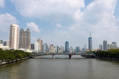 Nehrin kıyısında park alanları olan bir köprü. Arka planda gökdelenler ve binalar var. Çin, Guangzhou