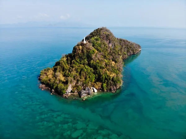 Aerial view of a lonely rocky island covered with greenery in the middle of the sea. Theres a building on top of the island