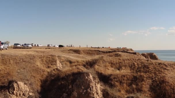 View of clay mountains near the Dnieper estuary. Many tourists walk on the rocks. Tents are set up and cars are standing. Stanislav, Ukraine. — Stock Video