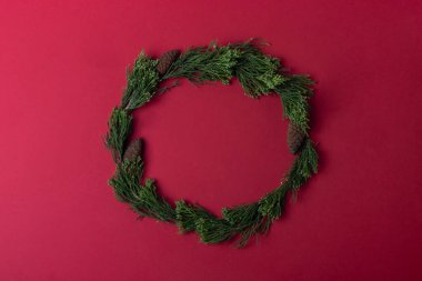 Kırmızı arka planda yeşil kozalaklı çelenk. Noel konsepti