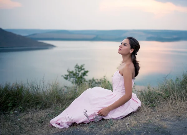 Chica en un vestido sentado en una roca junto al río — Foto de Stock