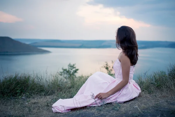 Chica sentada en la orilla del río y mirando el atardecer — Foto de Stock