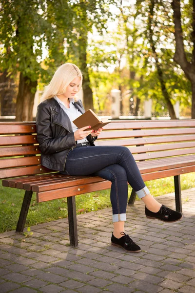 Hermosa chica sentada en un banco y leyendo un libro — Foto de Stock