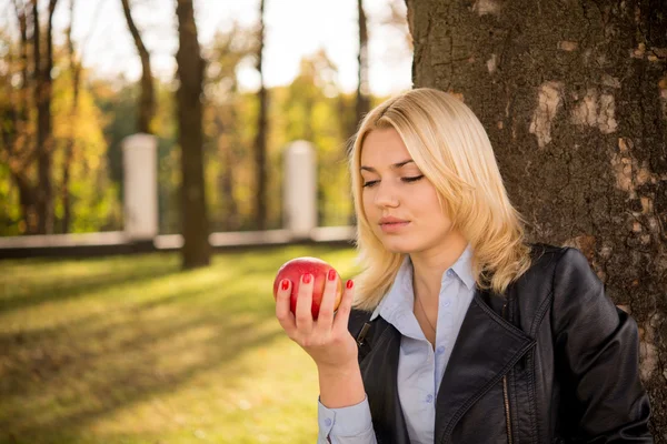 Красивая девушка стоит рядом с деревом и смотрит на яблоко в ней — стоковое фото