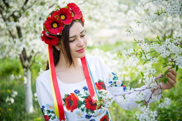 Girl in national dress among flowering branches — Stockfoto