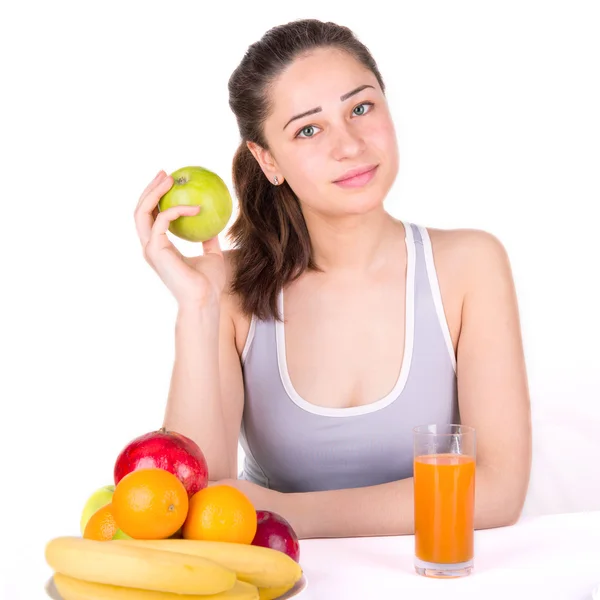 Девушка сидит рядом с фруктами и держит яблоко — стоковое фото