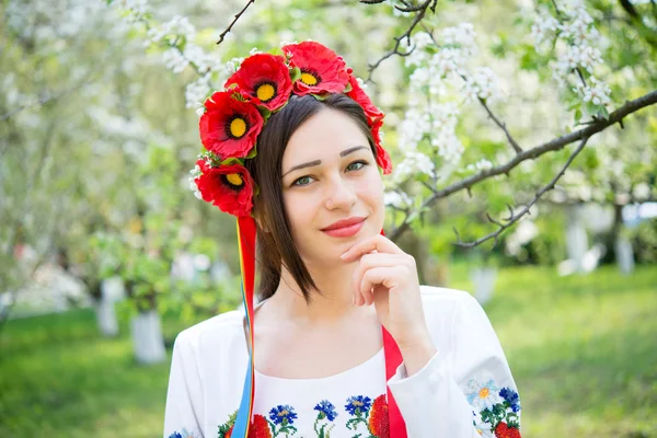 Smiling girl in national clothes in a flowering garden — Zdjęcie stockowe