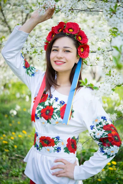 Smiling girl in national dress among flowering trees — Stockfoto