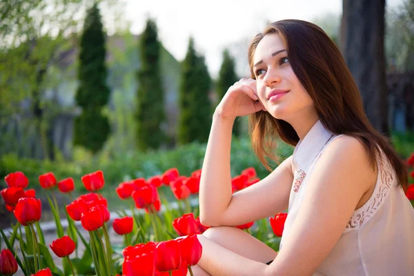 Chica pensativa sentada cerca de tulipanes rojos — Foto de Stock