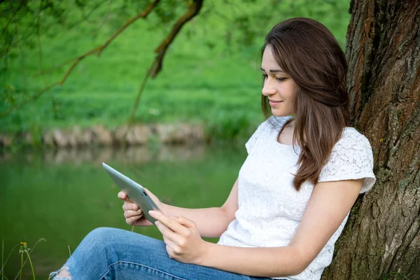 Девушка держит планшет, сидя под деревом — стоковое фото