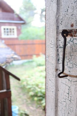 Büyük bir demir kanca soyulan ahşap kapılardan sarkıyor, ve kapı da köy evini gösteriyor.