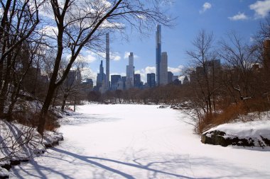 New York 'taki Central Park' ın karlı gölünün arkasındaki milyarder sırasının muhteşem gökdelenleri.