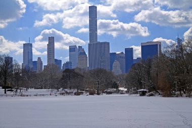 Bulutlu gökyüzü, muhteşem gökdelen ve New York 'taki Central Park' ta kar.