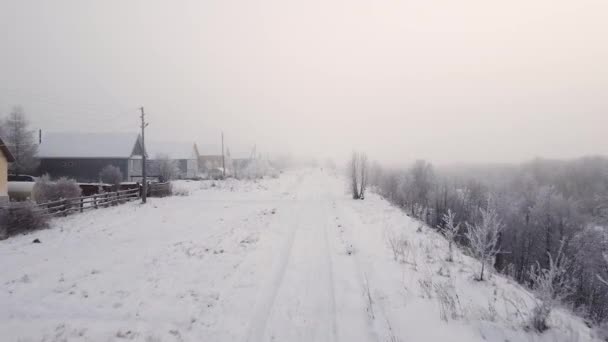 Ciężka śnieżna zima w wiosce na dalekiej północy, małe drewniane domki w śniegu, ciężka mgła. Widok z lotu ptaka, strzelanie z drona. — Wideo stockowe