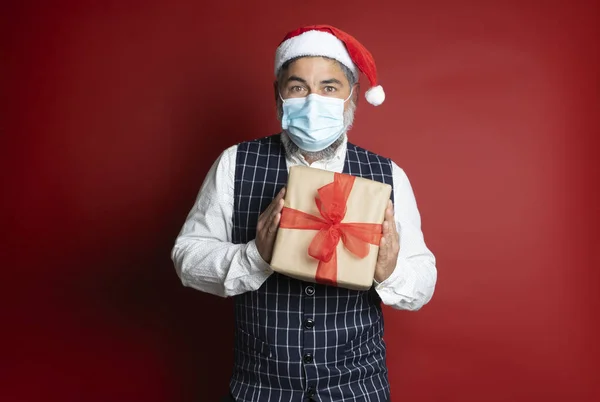 Человек Хирургической Маске Рождественской Шляпе Держит Иллюзией Подарочную Коробку Красном — стоковое фото