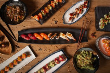 Restoran masasında çeşitli suşi, sashimi, nigiri, yakisoba ve edamame tabakları olsun.