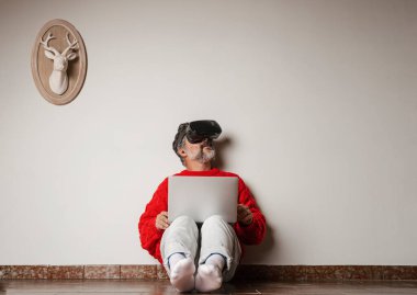 İnsan evde sanal gerçeklik deneyiminin tadını çıkarıyor. Sanal gerçeklik kulaklığı takan orta yaşlı beyaz bir adam yerde oturuyor. VR teknoloji kavramı