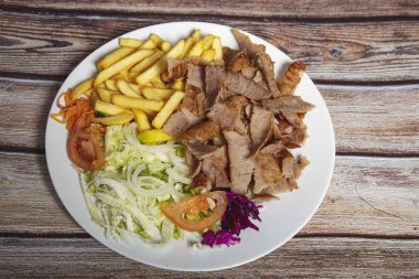 Beef doner on a plate with french fries and salad on wooden background. clipart
