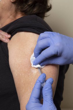 Hemşire iğneyi yaptıktan sonra yaşlı kadının koluna alkol çubuğu sürer.