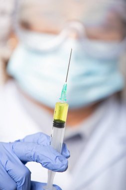 Sağlık ve salgın konsepti - gözlük, eldiven ve yeni aşı için şırınga ile koruyucu maske takan bir kadın doktora yakın çekim