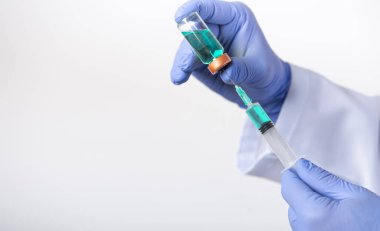 Doktorun eli şırınga ve aşıyı beyaz zemin üzerinde tutuyor.