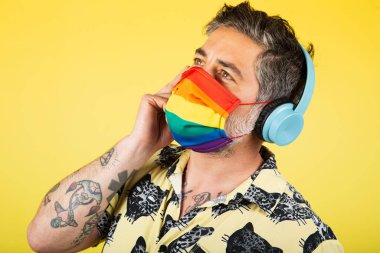 Adam müzik dinliyor ve koruyucu eşcinsel gurur maskesi takıyor. Coronavirus yaşam tarzı