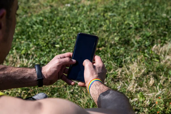 Elinde akıllı telefon tutan gay bayraklı bir adam.