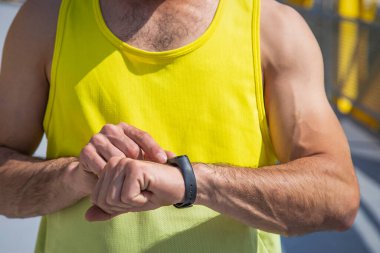 Genç sporcu ayakta dikilirken saati kontrol ediyor.