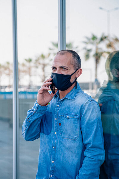 Middle-aged Latino man happily talking on the phone with face mask