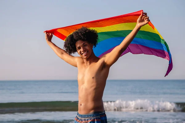 Kızıl saçlı, lgtbi bayrağı gösteren genç Latin bir adam.