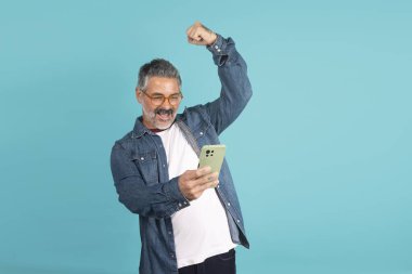 Olgun adam akıllı telefonuna bakarken kutlama yapıyor ve kazanıyor.