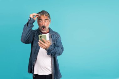 Olgun bir adam akıllı telefon tutarken şok ve şaşkınlıkla tepki verir.