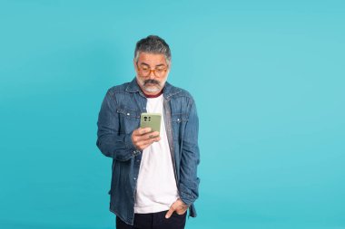 Gözlüklü, cep telefonu kullanan, temiz bir arkaplana odaklanmış yetişkin bir adam.