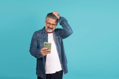 Olgun bir adam cep telefonu ekranına bakarken kafasını kaşıyarak kafa karışıklığı yaratıyor.