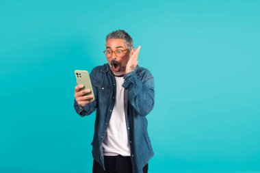 Adam donuk bir arka planda akıllı telefona şaşırmış ve şaşırmış görünüyor.