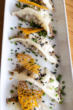 Gyoza köfteleri, susam tohumları ve soğanla süslenmiş beyaz servis tabağına dizilmiş.