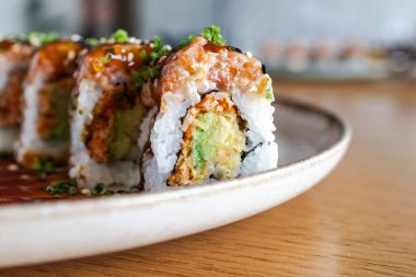 Somon, avokado ve seramik tabakta sosla kaplı suşi ruloları.