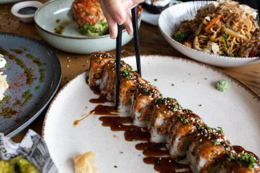 Yemek sırasında beyaz bir tabaktan lezzetli bir suşi rulosu seçiyorum.