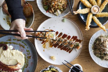 Yemek çubukları, Asya füzyon tabaklarıyla dolu bir masadan suşi rulosu toplamak.