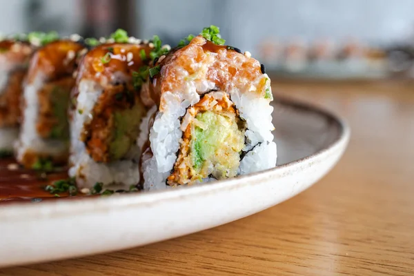 Somon, avokado ve seramik tabakta sosla kaplı suşi ruloları.