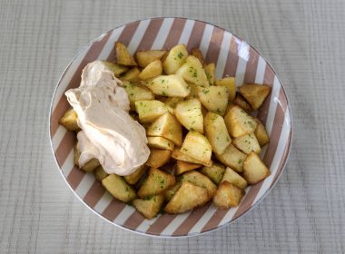 Patatas bravas kremalı baharatlı sos ve taze maydanoz garnitürlü kızarmış patates servis ediyor.
